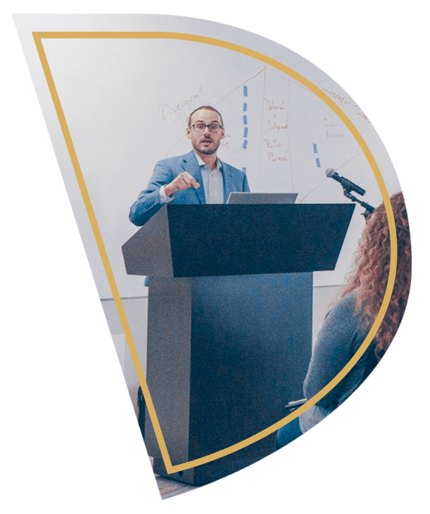 Image of Dr. Tad Dickel behind a podium presenting to a group. The image is cut out in the shape of a D with a gold frame around it.