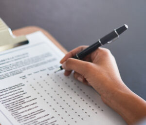 closeup photo of a woman's hand filling out a checklist survey on a clipboard